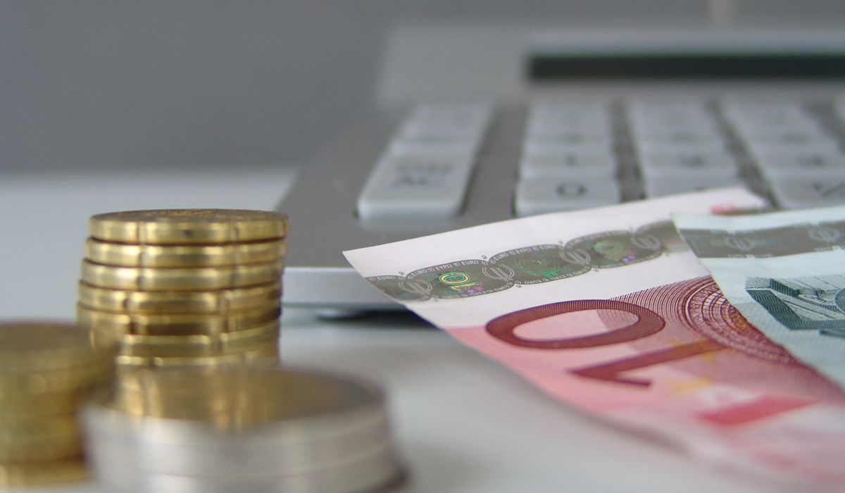 Baufinanzierungstipps Mehrere Stapel Euromünzen und Euro-Geldscheine liegen vor einer Computertastatur auf einem Tisch.